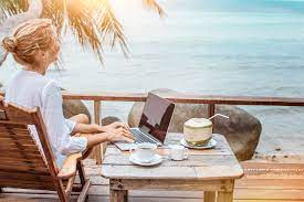 Женщина на фоне моря сидит за столом с ноутбуком и кофе